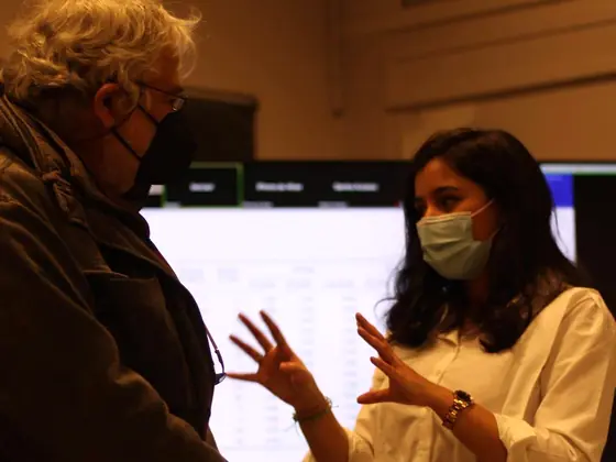 Douae Ahmadoun talking with a jury member at her PhD defense in Paris, a results table on the screen behind them